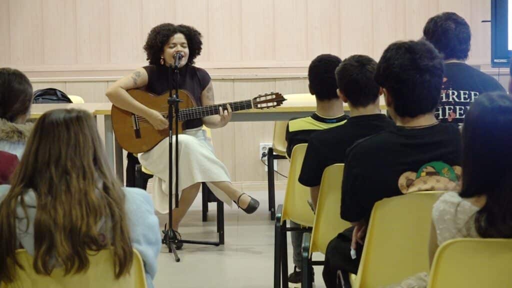 Una cantautora canta amb la guitarra davant d’alumnes en una sessió de Ciutats Defensores dels Drets Humans