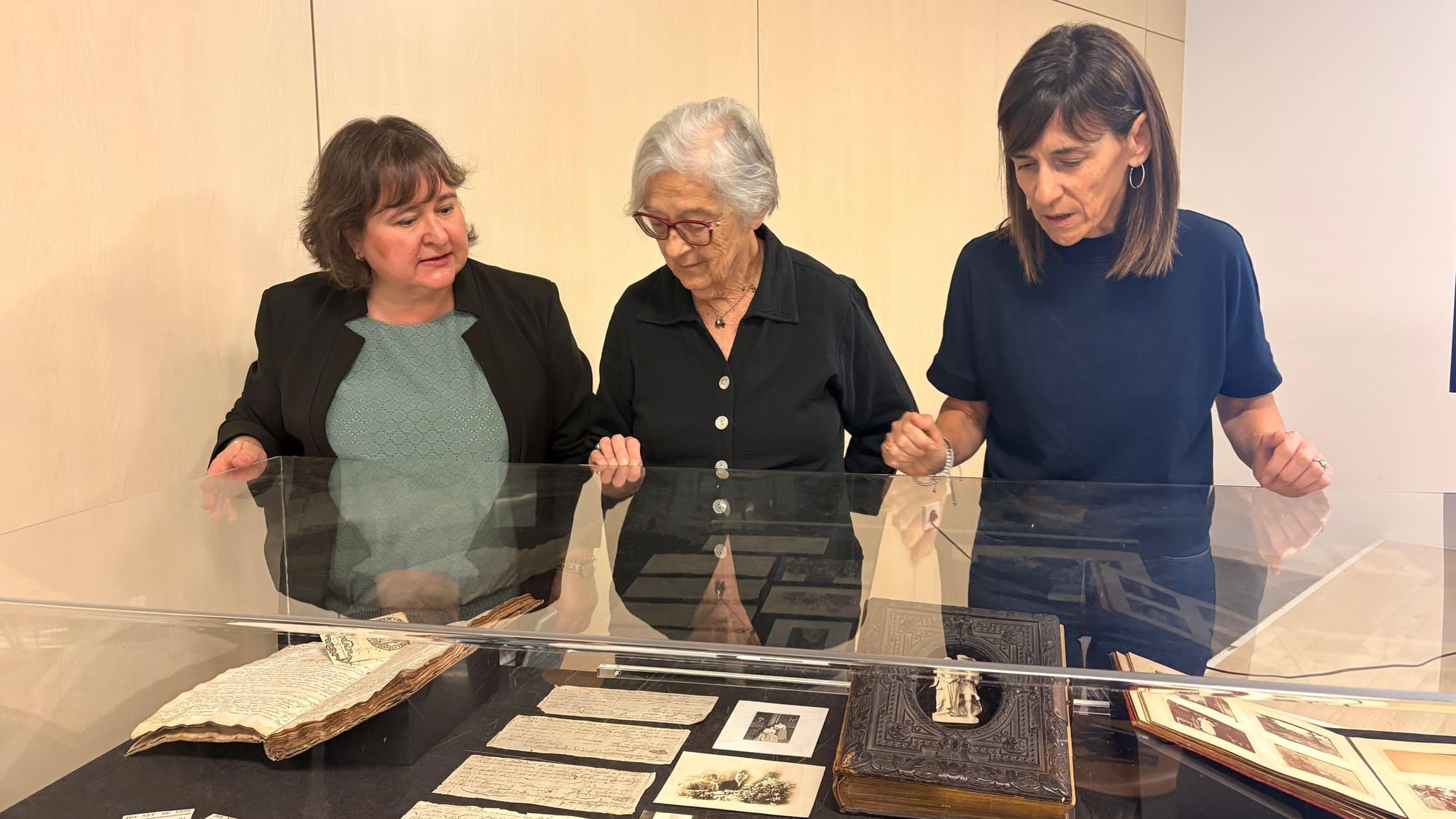 Tres dones observen documents i fotografies antigues del fons Felip Font Montaner en una vitrina de l’Arxiu Municipal de Reus