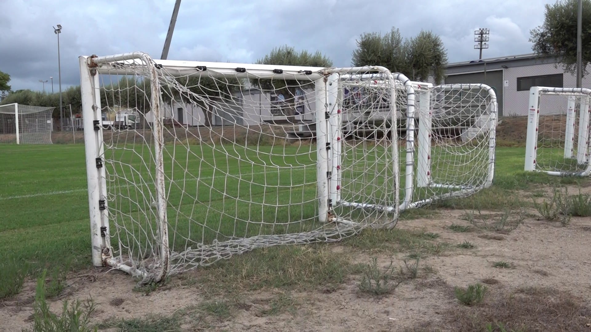 Porteries de futbol apilades al costat d’un camp de gespa sota un cel ennuvolat